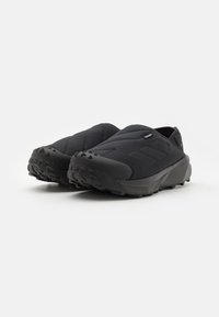 Black slip-on outdoor shoes with a quilted upper, textured rubber sole, and minimalist design featuring three horizontal stripes.