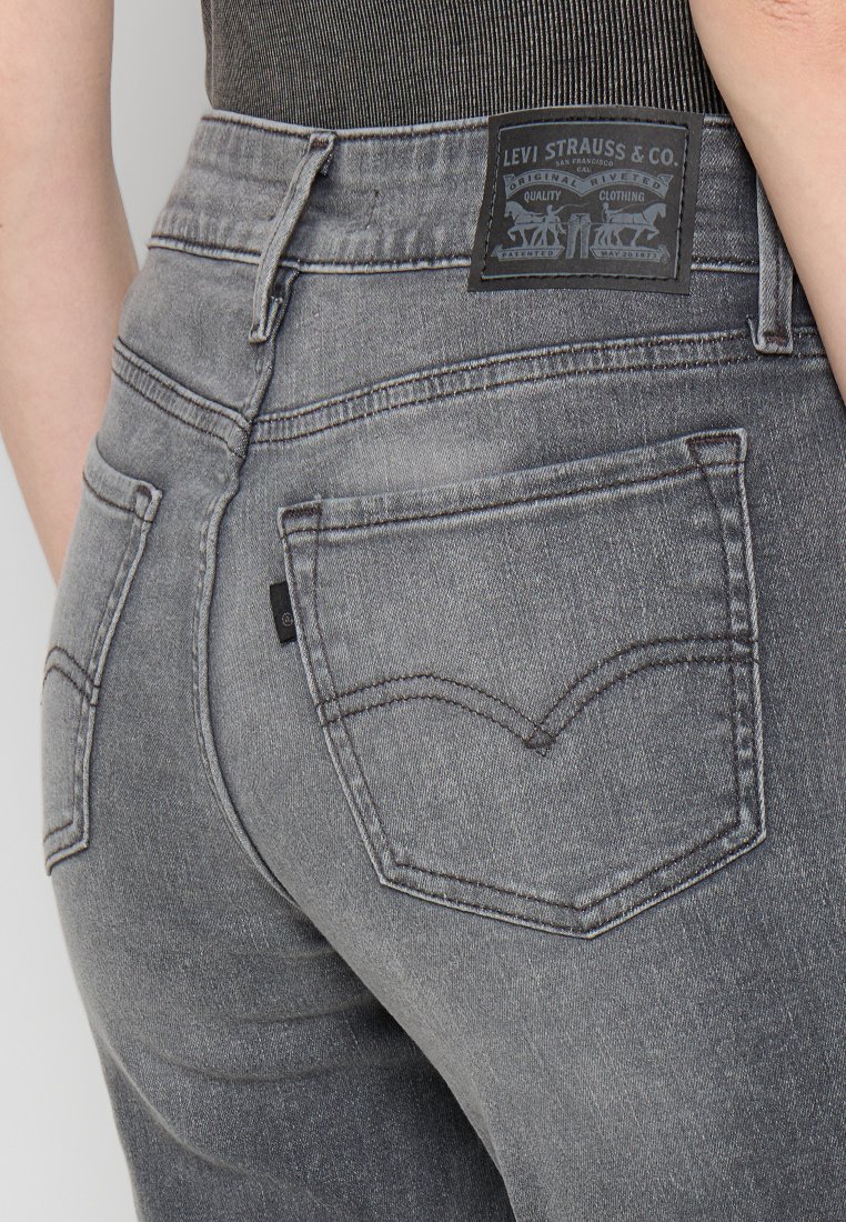 Jeans de mezclilla gris con un bolsillo trasero con costura distintiva, una etiqueta de marca de cuero y un diseño ajustado. Textura suave y tiro medio.