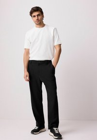 White textured short-sleeve shirt, black dress pants, and black sneakers with cream soles. Simple, fitted design with no visible patterns.