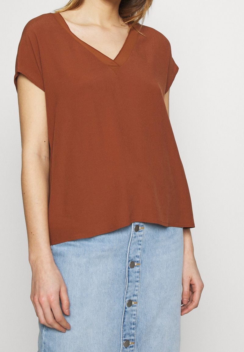 Haut rouille à manches courtes avec un décolleté en V, fabriqué à partir d'un matériau léger, associé à une jupe en denim bleu clair avec des boutons sur le devant.