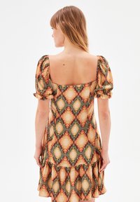 Robe à motifs floraux avec de courtes manches bouffantes, décolleté carré, jupe à volants, et motifs losanges orange, vert et crème. Texture de tissu douce.