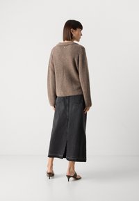 Pull brun, duveteux avec un col et des détails de boutons au dos, associé à une longue jupe en denim noir avec une fente centrale et un ourlet effiloché.