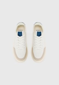 Zapatillas blancas con un diseño texturizado, acentos en beige, etiqueta de tela azul y detalles perforados en la puntera. Incluyen cordones y una suela lisa.