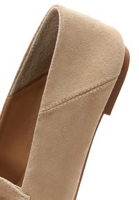 Beige Wildleder Slipper mit glatter Textur, leicht abgerundetem Zehenbereich und minimalistischem Design. Flache Sohle ohne sichtbare Beschläge.