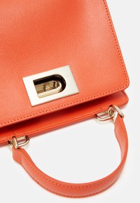 Sac à main en cuir texturé orange avec un fermoir rectangulaire doré et une courte poignée attachée par une quincaillerie dorée sur fond blanc.