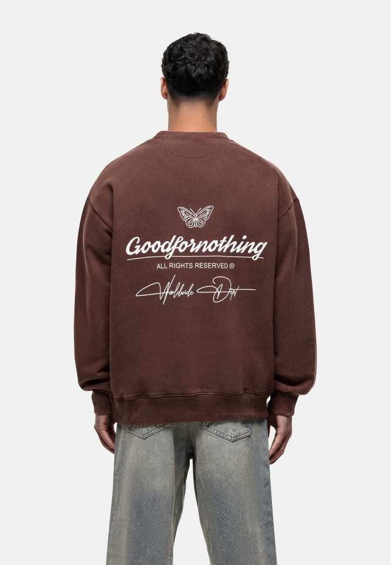 Felpa oversized marrone con una grafica di farfalla e il testo bianco "Goodfornothing" sulla schiena. Realizzata in tessuto morbido, presenta polsini a costine.