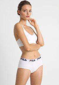 Set di reggiseno e mutandine bianche in cotone. Il reggiseno presenta un profondo scollo a V; le mutandine hanno un elastico con marchio e dettagli rossi e blu.