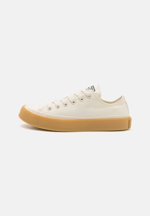 Baskets en toile couleur blanc cassé avec un bout rond, semelle en caoutchouc couleur miel, six œillets pour les lacets et une petite étiquette de logo sur la languette.