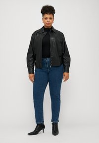 Black faux leather jacket with a collar, worn over a black top, paired with blue jeans and black pointed ankle boots.