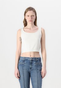 Top corto bianco con scollatura rotonda e orlo a costine, abbinato a jeans in denim blu a vita alta con tasche laterali e cuciture chiare.