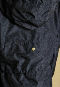 Giacca in tessuto scuro con motivo floreale, dotata di cappuccio, bottone a pressione dorato e fascia elastica in vita per una vestibilità sagomata.