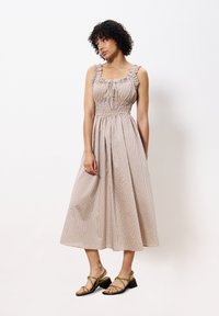 Gestreiftes Midi-Kleid aus weichem Stoff mit smockiertem Oberteil und Rüschenträgern. Sandbeige mit pastel Farben. Getragen mit grünen Sandalen mit Riemchen.