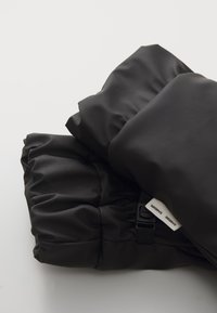 Black padded fabric item with a smooth, matte texture. Features gathered edges and a strap buckle. Includes a label with text.