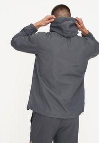 Dunkelgraue, leichte Kapuzenjacke mit elastischen Bündchen und lockerer Passform, die eine glatte Textur und ein dezentes, mattes Finish besitzt.