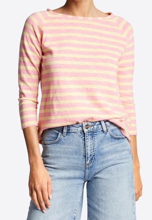 Frau trägt ein pink-gelb gestreiftes Langarmshirt, das in hoch taillierte, hellblaue Denim-Jeans gesteckt ist.