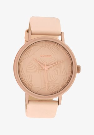 Montre ronde en or rose avec un motif de feuille de palmier en relief sur le cadran, aiguilles assorties et bracelet en cuir beige pâle.