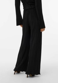 Zwarte geplooide broek met wijde pijpen en een hoge taille, voorzien van lange mouwen en een gestructureerde stof. Zoom licht uitlopend aan de onderkant.