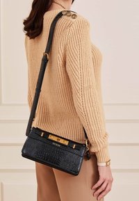 Musta keinonahkainen ristikkälaukku krokotiilimallilla, jossa kullanväriset metalliosat, suorakaiteen muotoinen ja brändätty lukko.