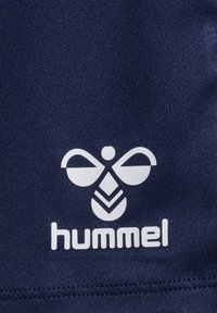 Hvid stiliseret bi-logo over ordet "hummel" på mørkeblåt tekstureret stof.