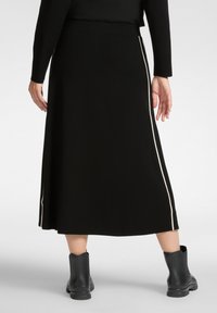 Zwarte midi rok met een aangesloten taille, voorzien van crèmekleurige zijstrepen langs de naden. De stof lijkt glad met een lichte glans.