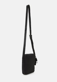 Borsa a tracolla nera realizzata in tessuto testurizzato, dotata di chiusura con zip, tracolla regolabile e dettaglio laterale con coulisse. Forma quadrata.