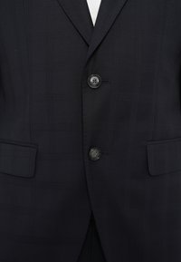 Tamsiai mėlynas languotas švarkas su iškirptu atlapu, dviem sagomis ir kišenėmis su atvartais. Lygios tekstūros, struktūruoto dizaino ir pritaikyto silueto.