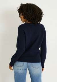 Suéter tejido azul marino con mangas largas, cuello redondeado y dobladillo acanalado, combinado con vaqueros de mezclilla azul claro. Textura suave, diseño sencillo.