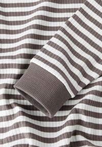 Zbliżenie na brązową i białą poziomo prążkowaną tkaninę z złożonym rękawem, który ma jednolitą brązową mankiet.