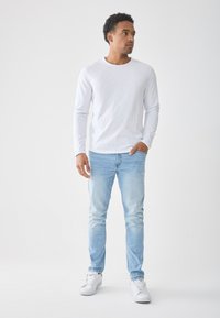 Fehér hosszú ujjú ing, világoskék farmer és fehér sportcipő. Slim fit szabású, kerek nyakkivágással; a farmer halványított mosással és öt zsebes kialakítással rendelkezik.