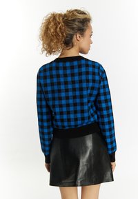 Maglione a scacchi blu e nero con colletto rotondo e polsini a costine neri, abbinato a una mini gonna di pelle nera. Tessuto testurizzato.