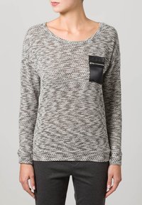 Stickad tröja i grått med ett texturerat mönster, rundad halsringning och en svart dragkedjeficka på vänster fram sida. Långa ärmar.