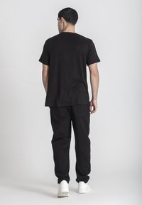 Čierne rebrované tričko a čierne nohavice s voľnejším strihom. Biele tenisky dotvárajú celý outfit. Hladká textúra s jednoduchým dizajnom.