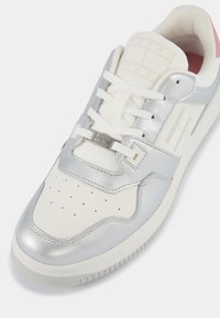 Sneaker argento e bianco con tomaia in pelle liscia, punta perforata, linguetta testurizzata e un accento rosa sul tallone. Presenta lacci e un dettaglio metallico.