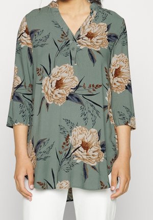 Bloemen tuniek in gedempte groene kleur met beige en marineblauwe bloemen. Voorzien van een V-hals, knopenlijst en driekwart mouwen. Zachte stof.