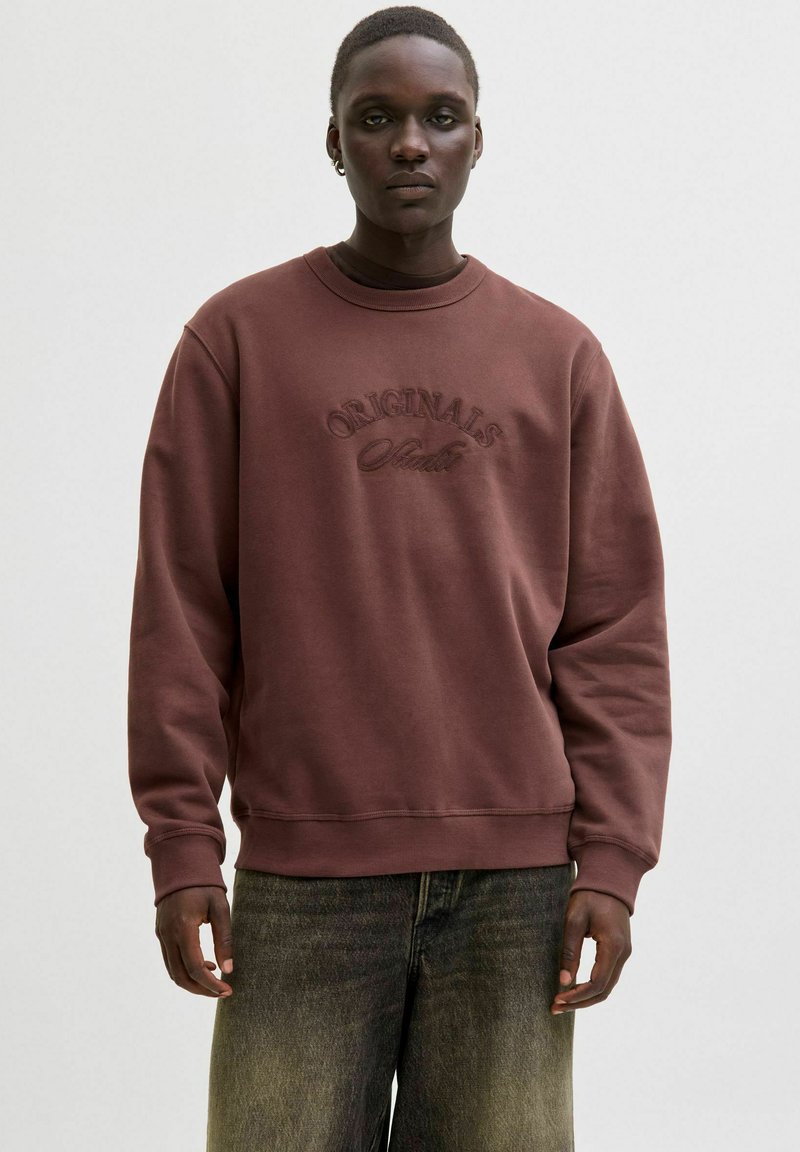 Brown sweatshirt with a crew neckline, featuring an embossed "ORIGINALS" logo. The fabric appears soft, with ribbed cuffs and hem.