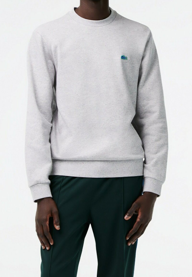 Sudadera gris de algodón, con cuello redondo y puños acanalados. Incluye un pequeño logo azul en el pecho. Tejido texturizado.