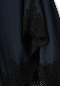 Tessuto navy con dettagli in pizzo nero intricati all'orlo, caratterizzato da bordi ondulati e frange, creando un contrasto testurizzato.