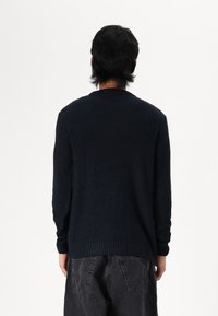 Suéter de punto azul marino con una superficie texturizada y dobladillo acanalado. Presenta mangas largas y un diseño de cuello redondo. Se muestra la vista trasera.