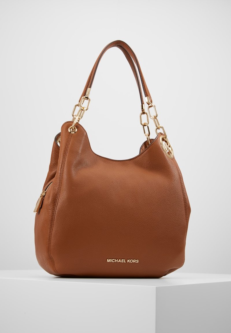 Sac à main Michael Kors en cuir marron avec double anse et maillons de chaîne dorés, exposé sur un socle blanc sur fond gris clair.