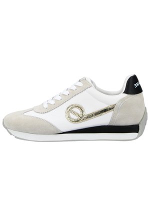 Baskets blanches et beiges avec des lacets blancs, un talon noir, une bande noire sur la semelle et un motif boucle métallique doré sur le côté.