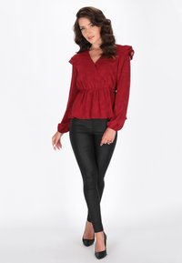 Rote Bluse mit Blumenmuster, rüschigen Ärmeln, gerafftem Taillenbereich und V-Ausschnitt, kombiniert mit schwarzen enger geschnittenen Hosen und High Heels.