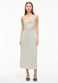 Robe midi de style débardeur en crème avec des pois noirs, présentant des bretelles fines et un corsage ajusté, se terminant juste en dessous du genou.