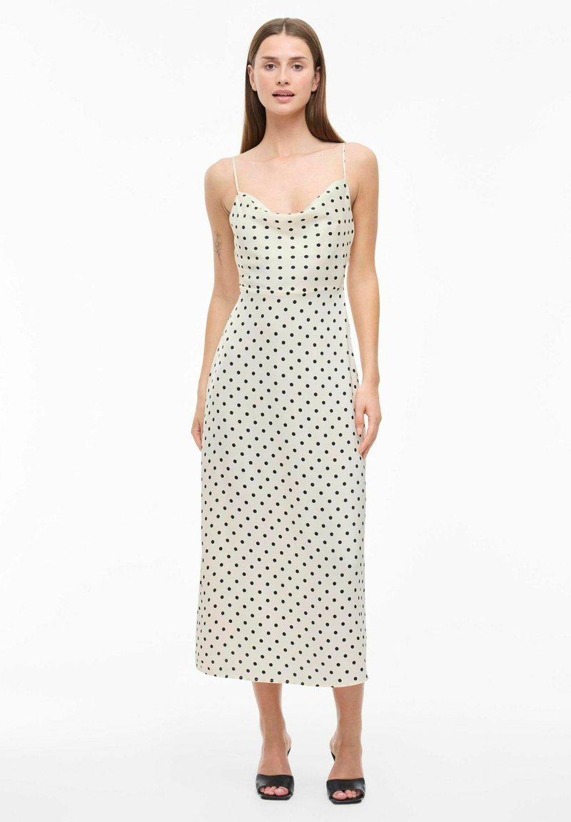 Robe midi de style débardeur en crème avec des pois noirs, présentant des bretelles fines et un corsage ajusté, se terminant juste en dessous du genou.