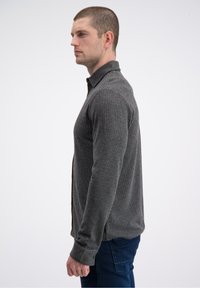 Szara prążkowana koszula z długim rękawem, kołnierzykiem na guziki, dopasowanym krojem i teksturowaną tkaniną, przedstawiona na modelu z boku.