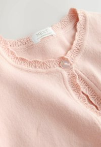 Jasnoróżowy kardigan z falbankowym dekoltem, z guzikiem przezroczystym i miękkim, teksturowanym materiałem. Metka brzmi "NEXT".