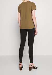 Top corto marrón de mangas cortas combinado con leggings negros ajustados. El calzado presenta tacones de tiras negros con un tacón de bloque de carey.