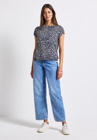 Top de manga corta con un patrón geométrico en navy y crema, combinado con jeans de pierna ancha en azul claro y zapatillas blancas.