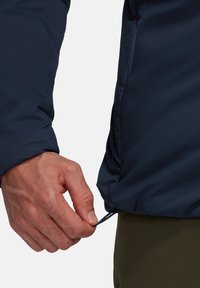 Mörkblå isolerad jacka med en slät yta, som har en justering med toggles vid nederkanten och en figurnära passform.