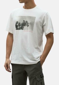 Camiseta de algodón blanca con un gráfico en blanco y negro de una palmera y el texto rojo "PORQUE NO HAY UN PLANETA B" debajo de la imagen.
