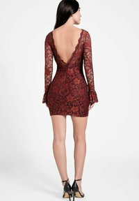 Robe rouge en dentelle à manches longues, dos en V et silhouette ajustée. Comprend des manches évasées aux extrémités et un motif floral texturé.